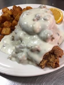 biscuit covered in sausage gravy with breakfast potatoes