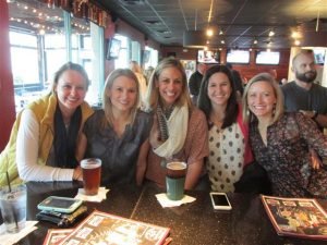 Five Women smiling by a table with two beers on top